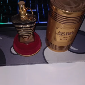 Jean Paul Gaultier Le Male Elixir tom flaska - Säljer en lyxig parfym, Le Male Elixir från Jean Paul Gaultier. Flaskan har en unik kroppsliknande form i guld och svart med en snygg ringdetalj vid halsen. Kommer med original guldfärgad burk och röd sammetsbas. Perfekt för dig som gillar exklusiva dofter. Helt tom