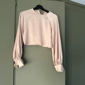 Beige croppad silkesblus NA-KD - Säljer en beige croppad blus från NA-KD med långa puffiga ärmar och breda manschetter. Fråga för fler bilder. 