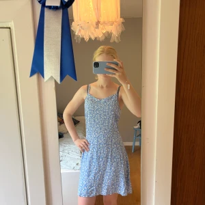 Blå blommig sommarklänning Primark - Supersöt blå kortklänning från Primark med vita små blommor och smala axelband. Lätt och luftig modell som passar perfekt till varma dagar. Klänningen har en feminin passform och är gjord i mjukt material.