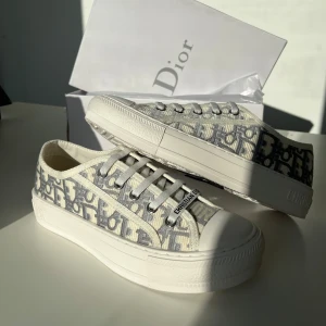 Dior Oblique sneakers i canvas - Snygga Dior Oblique sneakers i vit och grå canvas med ikoniskt mönster och tydlig Christian Dior-logga på sula och plös. Skorna har rund tå, platt sula och klassisk snörning. Perfekt för dig som vill ha en lyxig och trendig look.