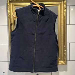Mörkblå manchesterväst  - Snygg mörkblå vadderad väst från Knowledge Cotton Apparel i manchester. Västen har hög krage, två stora fickor framtill och dragkedja hela vägen. Perfekt för en stilren look. Vid frågor är det bara att skriva🙌🏼🥂