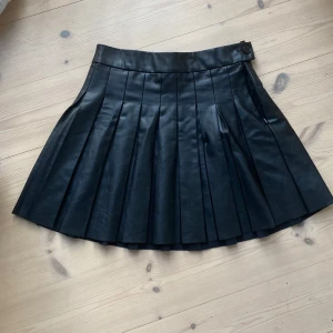 Svart kjol i fakeläder - Snygg kjol i fakeläder. Ganska kort på mig som är 172. Finns några små defekter som någon sprucken söm och små märken i lädret, men inget som märks på långt håll.