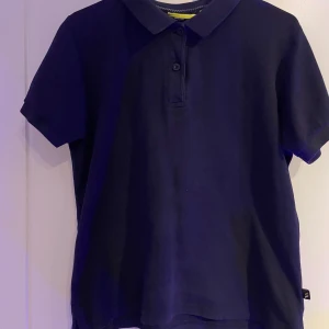 Mörkblå pikétröja Pro One S - Snygg mörkblå pikétröja från Pro One i storlek S. Klassisk krage, korta ärmar och knappar framtill. Tillverkad i funktionsmaterial som andas, perfekt för en aktiv livsstil. Enkel och stilren design utan mönster eller tryck.