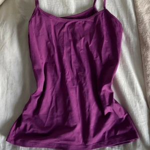 Lila linnetopp med smala axelband - En enkel och snygg lila linnetopp med smala axelband. Perfekt att styla med jeans eller kjol för en chill look. Toppens material känns mjukt och följsamt mot huden.