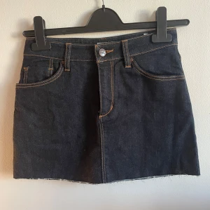 Mörk jeanskjol från Dobber - Snygg mörkblå jeanskjol från Dobber med klassiska fickor fram och bak, rå kant nertill och kontrastsömmar. Kjolen har normal passform och bälteshällor, perfekt till en enkel topp eller hoodie.