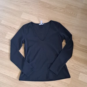 Svart långärmad topp med v-ringning - En stilren svart långärmad topp med djup v-ringning. Modellen är figurnära och passar perfekt till jeans eller kjol. Tillverkad i mjukt material som känns skönt mot huden. Enkel och snygg baströja för dig som gillar minimalistisk stil.💕