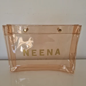 Transparent necessär från Neena Swim - Säljer en transparent necessär från Neena Swim i rosa plast med guldiga tryckknappar. Perfekt för blöta badkläder eller för att hålla koll på småprylar och smink. 