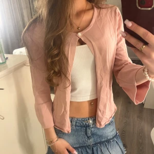 Ljusrosa kofta från More & More - Supersöt ljusrosa kofta från More & More i mjuk bomull. Koftan har långärmade trumpetärmar och en knapp framtill vid halsen. Superfin både stängd och öppen! :)