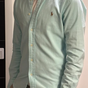 Ljusblå skjorta Polo Ralph Lauren S - Snygg ljusblå skjorta från Polo Ralph Lauren i slim fit-modell. Klassisk button-down krage, broderad logga på bröstet och stretchigt. Perfekt för dig som gillar stilrena och fräscha plagg med en exklusiv känsla.