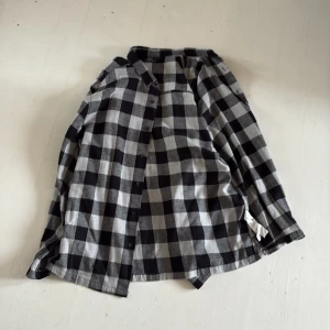 Rutig skjorta från Bershka i svart och grå - Säljer en snygg rutig skjorta från Bershka i svart och grå. Skjortan har klassisk krage, knäppning framtill och långa ärmar. Regular fit och tillverkad i mjukt bomullstyg. Perfekt för en chill och avslappnad stil.