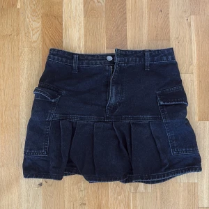 Svart jeanskjol med fickor och volang - Cool svart jeanskjol med stora fickor på sidorna och bred volang nedtill. 