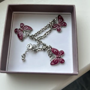 Silverfärgat armband med lila fjärilar - Snyggt armband i silverfärgad metall med flera hängen formade som lila fjärilar. Storleken går att ändras