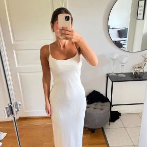 Vit satinlänning med smala axelband - Säljer en elegant vit satin långklänning med smala axelband och figurnära passform. Klänningen har en mjuk, glansig yta och enkel design som ger en stilren look. Perfekt för dig som gillar minimalistiskt och trendigt. Passar dig som har storlek 34 & 36!