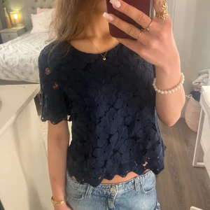 Mörkblå blommig blus Holly & Whyte - Supersöt mörkblå blus från Holly & Whyte med stora blommiga spetsdetaljer. Mycket fin tröja som använts fåtal gånger. Det är även dubbeltyg och väldigt fin passform. Köpte för 300 kr på plick men säljer för mycket bra pris :)