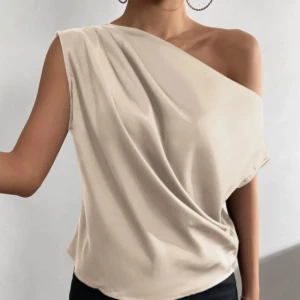 Champagnefärgad oneshoulder topp - Snygg champagnefärgad topp med oneshoulder-design och draperad effekt. Tunt, glansigt material som ger en lyxig känsla. Perfekt för dig som vill sticka ut med en stilren och modern look.