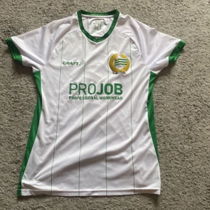 Hammarby IF matchtröja Craft vit/grön - Säljer en officiell Hammarby IF fotbollströja från Craft. Tröjan är vit med tunna gröna ränder, gröna detaljer vid ärmslut och krage samt klubbmärke på bröstet. Materialet är lätt och andas, perfekt för match eller träning. Sponsorlogga PROJOB på framsidan. Storleken är medium men passar även small.