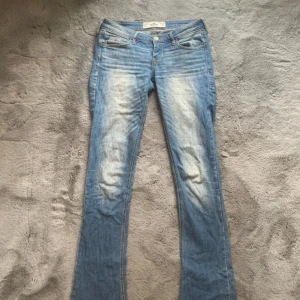 Blå bootcut jeans från Hollister - Snygga vintage lågmidjade ljusblå bootcut jeans från Hollister med slitningar och blekta partier framtill och baktill. Klassisk femficksmodell med låg midja och detaljerade bakfickor. Otroligt snygga men tyvärr lite för stora för mig