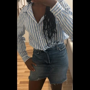 Blåvit randig skjorta från Lindex - Snygg blå och vit randig skjorta från Lindex i storlek 40. Skjortan har klassisk krage, långa ärmar och knappar framtill. Tillverkad i mjuk bomull och kan bäras både instoppad eller knytas framtill för en mer avslappnad look.