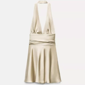 Champagnefärgad satin klänning XS - Supersnygg kort klänning i champagnefärgad satin från Zara. Djup v-ringning, omlott med knyt i ryggen och halterneck. Materialet är glansigt och mjukt, perfekt för dig som vill sticka ut. Passformen är normal och kjolen har ett fint fall.