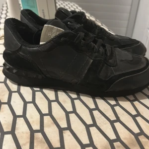 Svarta Valentino Rockrunner sneakers - Snygga svarta Valentino Rockrunner sneakers med coola nitar på hälen och mix av skinn och mocka. Klassisk rund tå, snörning och chunky sula ger en edgy vibe. Perfekta för dig som gillar streetstyle och exklusiva märken.