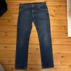 Mörkblå jeans från Nudie - W33 L32 (fungerar för de flesta med skärp) Säljer ett par klassiska blå jeans från Nudie med slim fit passform. Jeansen har fickor, snygga kontrastsömmar och Nudie-loggan broderad på bakfickorna. Perfekta för dig som gillar en tidlös och clean look. 