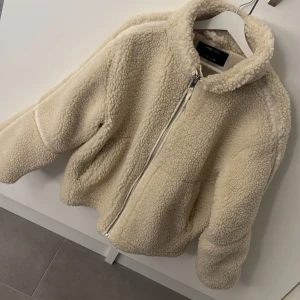 Beige teddyjacka M - Supermjuk och fluffig teddyjacka från Sinsay i beige färg. Jackan har hög krage, dragkedja framtill och två fickor. Perfekt för kyliga dagar och ger en vibe till din outfit.