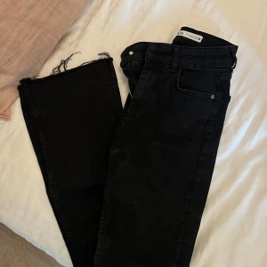 Svarta jeans med råa kanter från Zara bootcut full längd  - Svarta jeans från Zara i storlek 34 med trendiga råa kanter nertill. Klassisk femficksmodell med hög midja och smal passform. Perfekta för en edgy och stilren look.