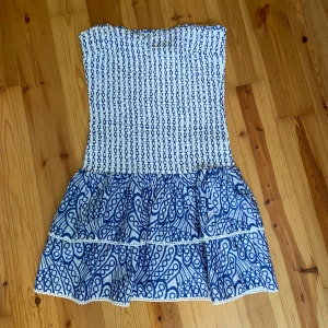 Vit och blå tubklänning från Gina Tricot - Supersöt axelbandslös kortklänning från Gina Tricot i vitt och blått. Smockad överdel och volangig kjol med coolt grafiskt mönster. Perfekt för varma dagar och sommarhäng. Lätt och luftig känsla! Storlek 146-152 men passar mig som vanligtvis har xxs/xs