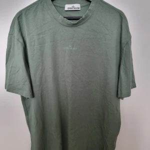 Grön t-shirt från Stone Island - Snygg grön t-shirt från Stone Island med diskret logga broderad på bröstet och tryck på ryggen. Klassisk passform med rund hals och korta ärmar. Perfekt för dig som gillar stilrena plagg med streetkänsla.