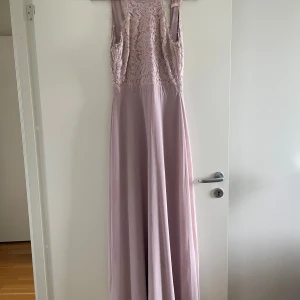 Ljusrosa långklänning från Only Eve - Superfin ljusrosa långklänning från Only Eve med spetsdetaljer upptill och öppen rygg. Klänningen har en elegant, ärmlös design och är tillverkad i mjuk polyester. Perfekt för bal eller student! Säljes då den inte längre kommer till användning. Saknas en knapp. 