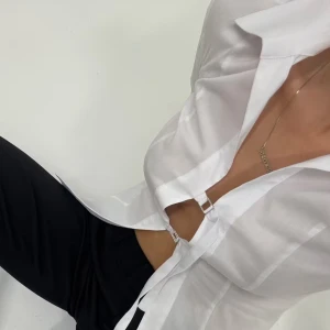 Vit skjorta med metallspännen från Bikbok - Säljer en vit långärmad skjorta från Bikbok med unik design – framtill stängs den med två silvriga metallspännen istället för knappar. Skjortan har klassisk krage och är tillverkad i ett tunt, lätt material som ger en fräsch och modern look.