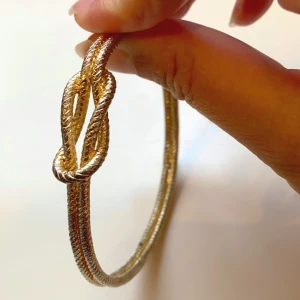 Guldigt armband med knutdetalj - Snyggt armband i guldton med repmönstrad yta och en cool knutdetalj framtill. Armbandet är stelt och har en stilren, modern känsla som passar perfekt till din outfit. Enkel att matcha och ger en trendig touch.