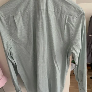 Ljusgrön mönstrad skjorta från Riley - Snygg ljusgrön skjorta från Riley i regular fit med diskret småmönstrat tryck. Skjortan har klassisk krage, långa ärmar och knäppning framtill. Perfekt för dig som vill ha en stilren look med lite extra detalj.