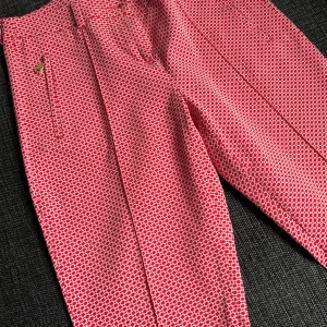 Rosa mönstrade byxor Marina Yachting - Snygga croppade byxor från Marina Yachting i rosa och vitt med ett tätt grafiskt mönster. Byxorna har smal passform, dragkedja och knapp framtill samt fickor med diskret detalj. Perfekta för dig som vill sticka ut lite extra.