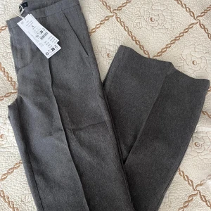 Grå kostymbyxor från GinaTricot - Snygga grå kostymbyxor från Gina i flared modell. Byxorna har pressveck, sidfickor och en diskret bakficka. Perfekta för dig som gillar en clean och klassisk vibe. Säljs pga köpt fel storlek 