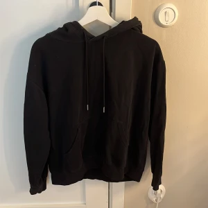 Svart hoodie från H&M Basics - Svart hoodie från H&M Basics med klassisk känguruficka och justerbar huva med snörning. Tröjan har lång ärm och är gjord i mjuk bomullsmix som är skön att ha på sig. Perfekt för chill dagar eller när du vill ha en enkel och stilren look. Hoodien är i storlek S men tycker att den har lite av en over sized känsla som gör den väldigt passande till hösten!