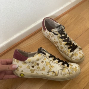 Golden Goose superstars med hjärtan - Golden Goose superstars i vitt med guldiga hjärtan, skorna är andvända i gott skick och är i storlek 36(endast skor medföljer i köpet)