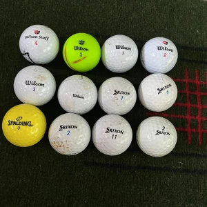 Mix av golfbollar (12-pack) - Bilden visar ett set med golfbollar från olika märken som Wilson, Srixon och Spalding. Perfekt för dig som gillar sport och vill ha extra bollar till golfträningen eller rundan. Flera bollar har olika färger och nummer, vilket gör det enkelt att hålla koll på dem under spelet.