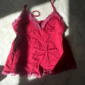 Röd linnetopp med spetsdetaljer - Supersöt röd linnetopp med tunna axelband och v-ringning. Toppen har fina spetsdetaljer i matchande röd nyans längs både urringning och nederkant. Perfekt för lager på lager eller som statement-piece. Mjuk och skön bomullskänsla.