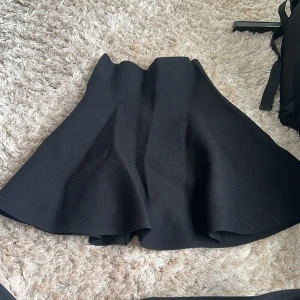 Svart kortkjol från Noisy May - Säljer en svart kortkjol från Noisy May med snyggt utsvängd form. Kjolen har en synlig dragkedja bak och är gjord i ett mjukt, lite tjockare material som känns skönt mot huden. Perfekt att styla med boots eller sneakers för en cool look.