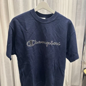 Vintage Champion t-shirt - Snygg mörkblå t-shirt från Champion med klassisk broderad logga över bröstet. T-shirten har rund halsringning och korta ärmar. Tillverkad i mjuk bomull.