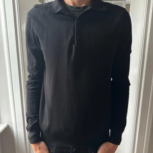 Svart långärmad pikétröja  - Klassisk svart slim fit pikétröja från h&m med lång ärm och krage. Tröjan har tre knappar framtill och är tillverkad i ett mjukt material som känns skönt mot huden. Perfekt för dig som gillar en clean och stilren look. Säljer för den är för liten. Modellen är 194cm 82kg. Hör av er vid frågor 