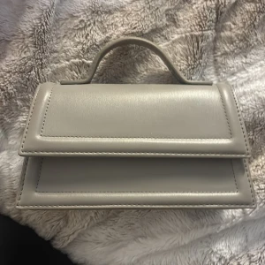 Grå handväska  - Grå handväska i skinn. Väskan har ett topphandtag och raka linjer som ger en clean look. Perfekt för dig som gillar minimalistiska accessoarer.