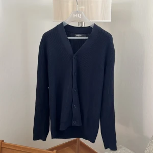 Mörkblå kofta från Dressmann L - Klassisk mörkblå kofta från Dressmann i storlek L. Den är ribbstickad med v-ringning och knäppning framtill med fem knappar. Perfekt att slänga över en t-shirt eller skjorta för en clean look. Materialet känns mjukt och passar året runt.