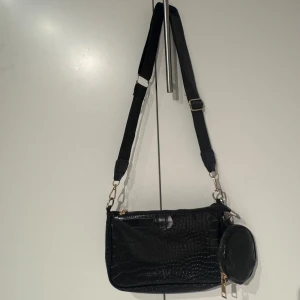 Svart axelväska - Snygg svart axelväska med krokodilpräglat mönster och bred justerbar axelrem. 