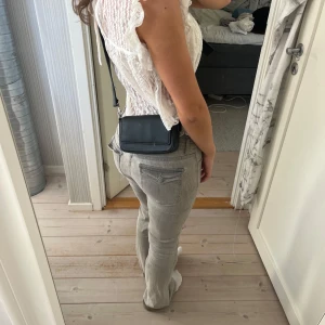 Svart axelväska i skinnimitation - Säljer en stilren svart axelväska i skinnimitation med rektangulär form och bred axelrem. Väskan har silvriga metalldetaljer och minimalistisk design. Enkel att matcha med olika outfits och passar till många tillfällen. Lite sliten på ena knäppet. 