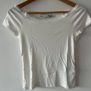 Vit spetskantad topp från 157 - Supersöt vit topp från lager 157 med korta ärmar och fina spetsdetaljer längs halsringning och ärmslut. Toppens enkla design gör den lätt att matcha och den har en mjuk, skön känsla mot huden. Perfekt för dig som gillar en clean och feminin stil.