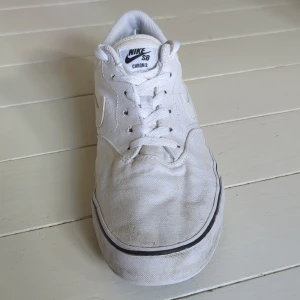 Vita Nike SB Chron 2 sneakers - Nike SB Chron 2 sneakers i helvitt med klassisk swoosh på sidan. Skorna har lågt skaft, snörning och en platt sula med svart rand. Ovandelen är i canvas och insidan har mjuk vaddering för extra komfort. Perfekta för skate eller streetstyle.