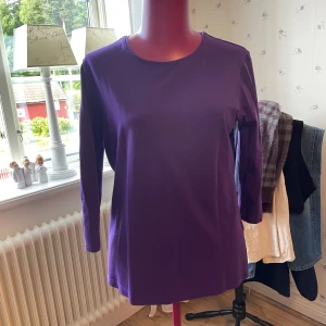 Lila topp från Joy of Love, 3/4-ärm - Säljer en lila topp från Joy of Love i storlek M. Modellen har rund halsringning och 3/4-ärm. Tillverkad i mjuk bomull med lite stretch. Perfekt till jeans eller kjol för en färgklick i garderoben.