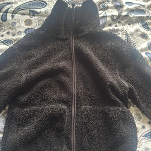 Svart teddyjacka i XS med dragkedja - Mysig svart teddyjacka i storlek XS med hel dragkedja framtill och två stora fickor. Jackan har hög krage och passar till allt.